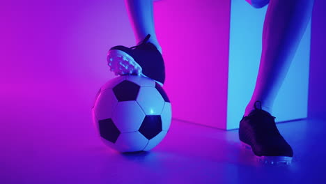 Close-up-of-the-foot-of-a-professional-black-football-player-standing-on-the-ball-in-slow-motion-in-the-blue-red-neon-light-of-the-studio.-Brazilian-football-player-foot-on-the-ball-to-pose